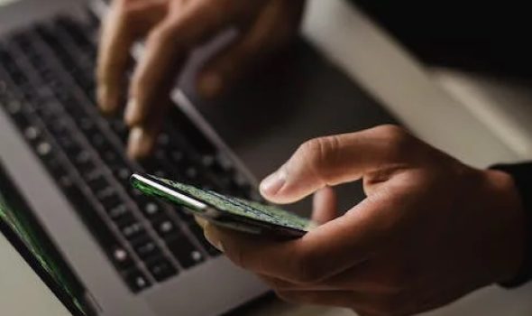 Hands holding a phone and typing on a laptop